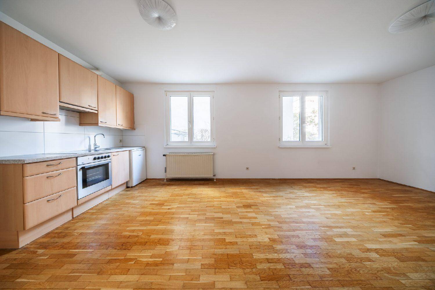 Offene Küche mit Holzschränken, Einbauherd und Parkettboden in einem hellen Raum.