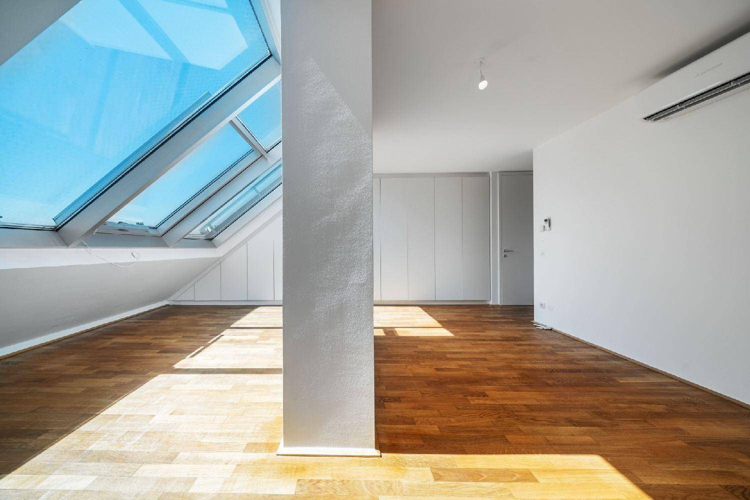 Heller Raum mit Holzboden, Dachschrägen, großen Dachfenstern und integrierten Schränken.