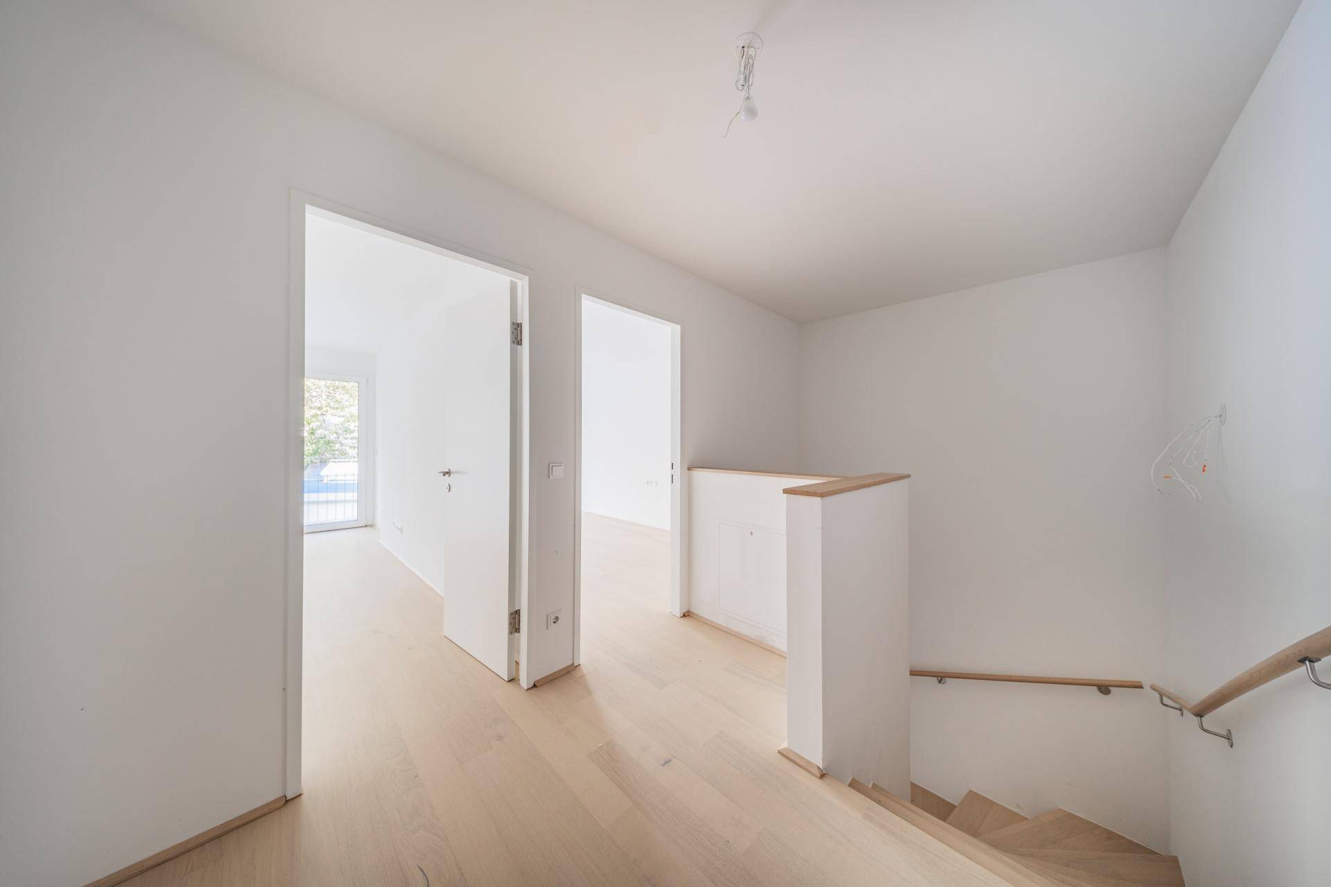 Heller Flurbereich im Obergeschoss mit Holzboden und einer Holztreppe, die zu den unteren Etagen führt.