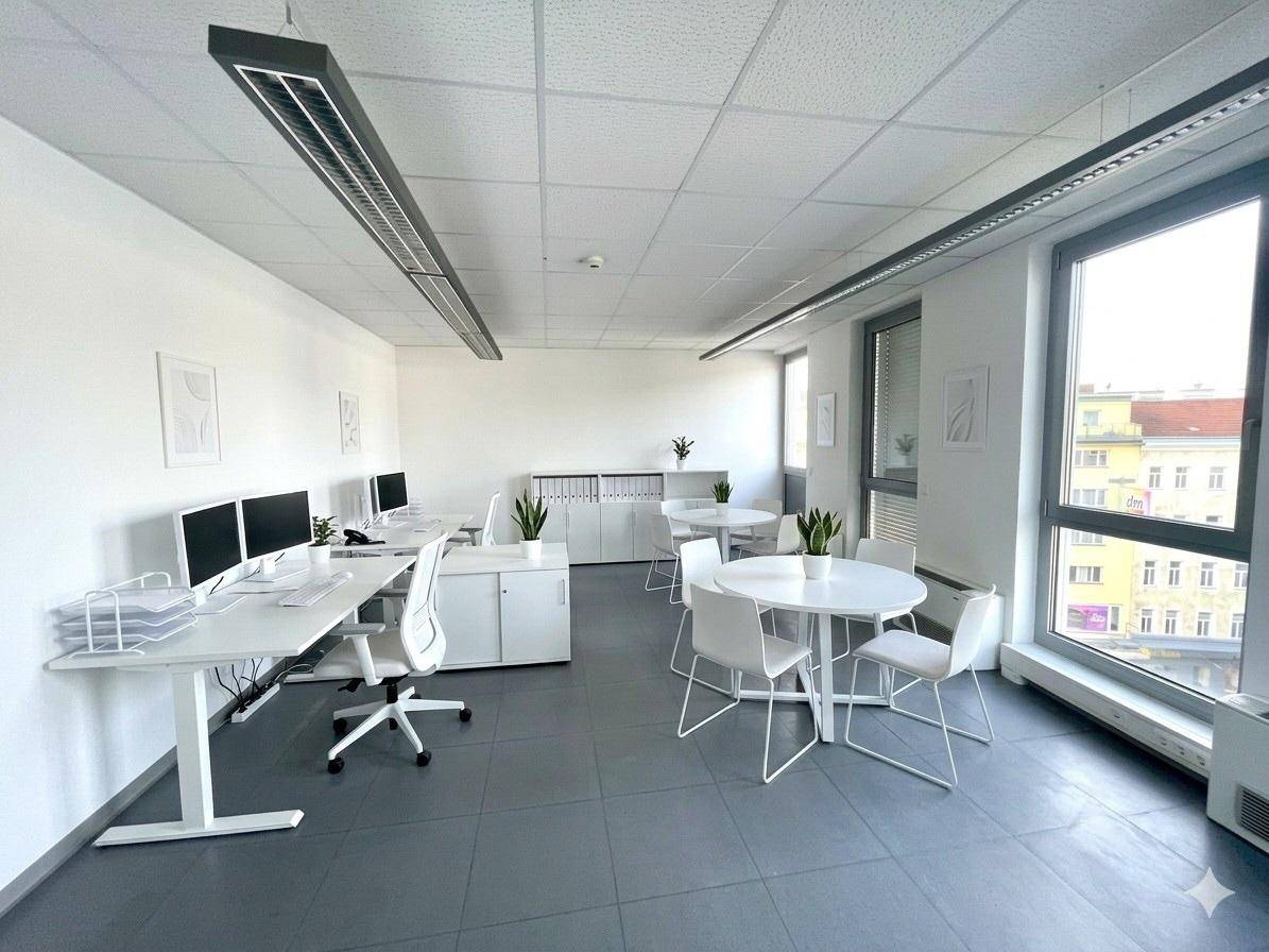Großes, helles Büro mit mehreren Arbeitsplätzen, einer Besprechungsecke und raumhohen Fenstern, auf Fliesenboden.