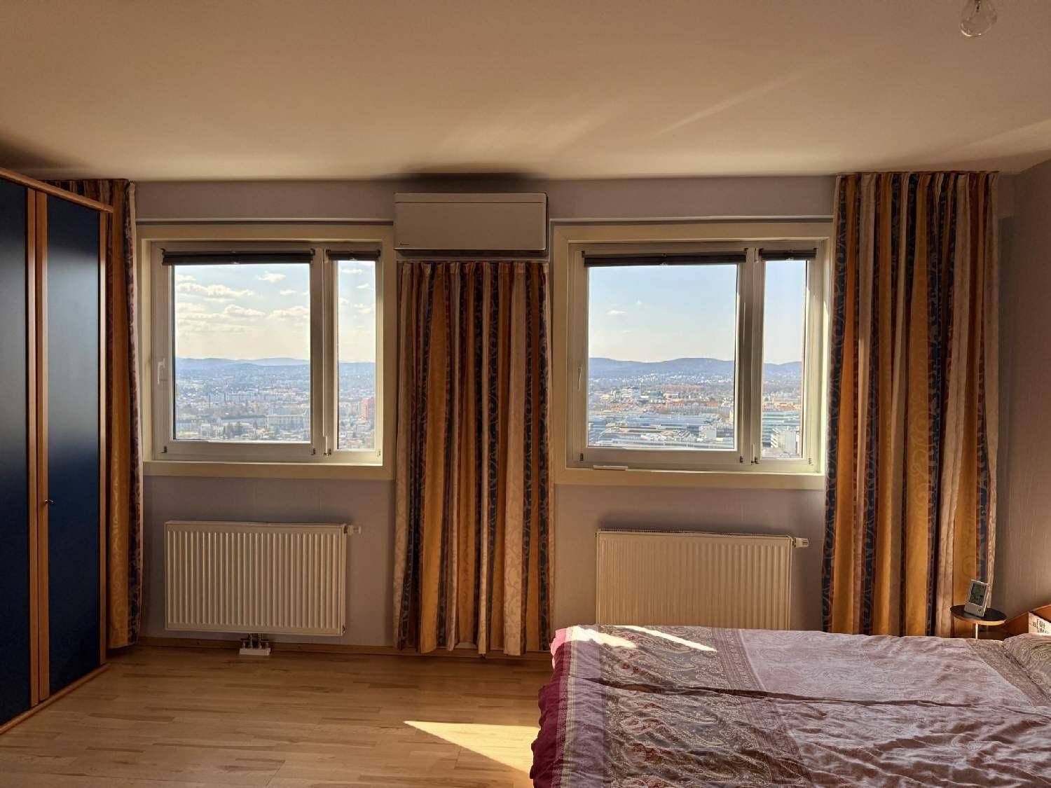 Schlafzimmer mit Doppelbett, Kleiderschrank und weitem Blick über die Stadt.