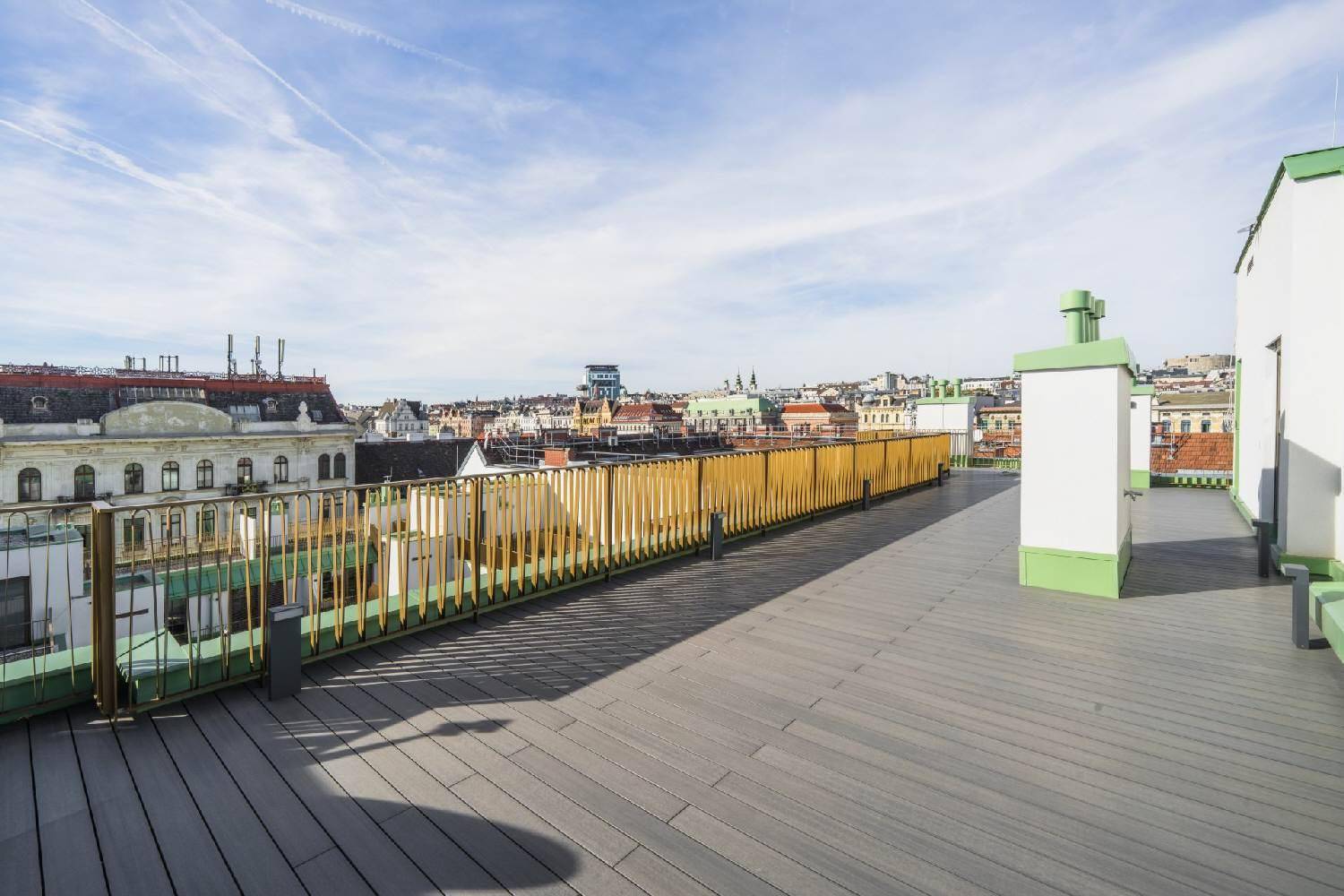 Lange Dachterrasse mit Holzboden und goldfarbenem Geländer, die einen Panoramablick bietet.
