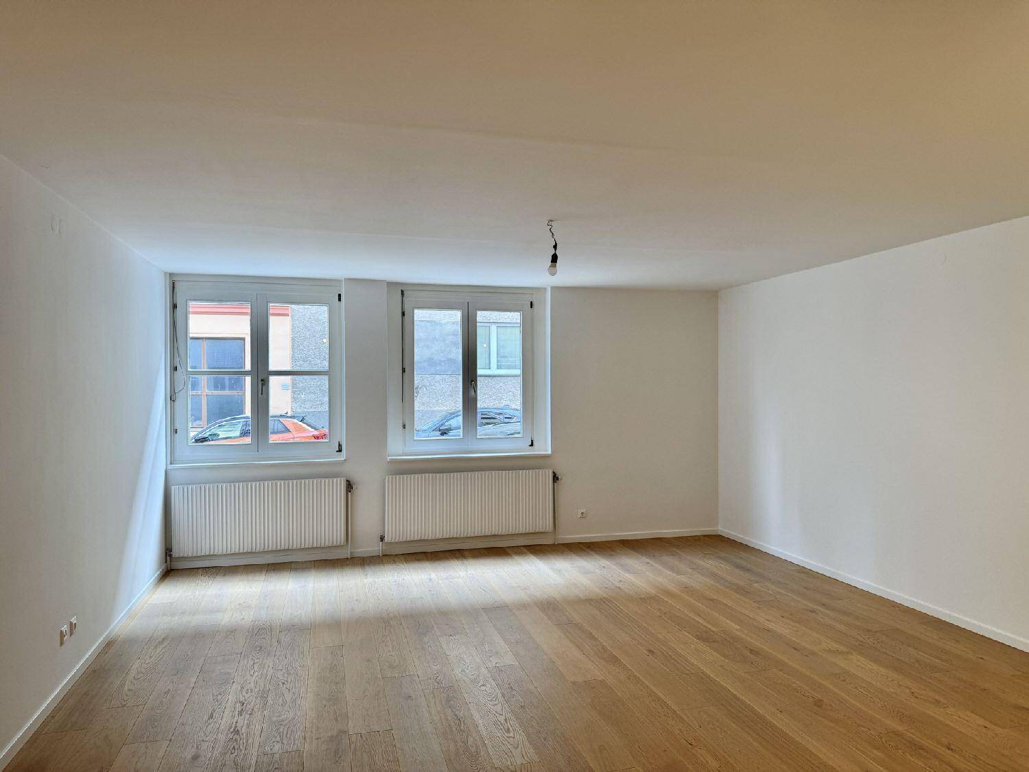 Geräumiges Zimmer mit hellem Parkettboden und großen Fenstern, ideal für Wohnzwecke.