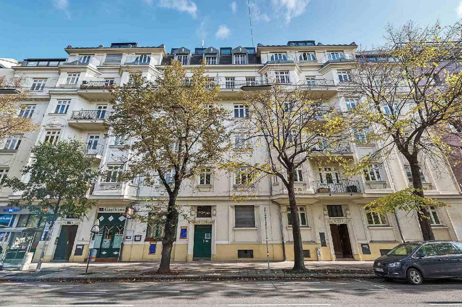 Klassische Fassade eines Wohngebäudes mit Geschäften im Erdgeschoss und Bäumen davor.