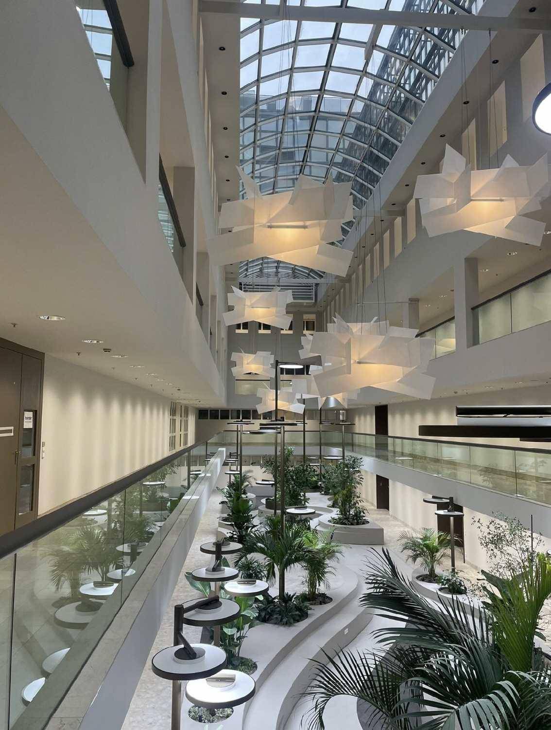 Helles und offenes Atrium mit viel Grün, modernen Designleuchten und einem weitläufigen Glasdach.