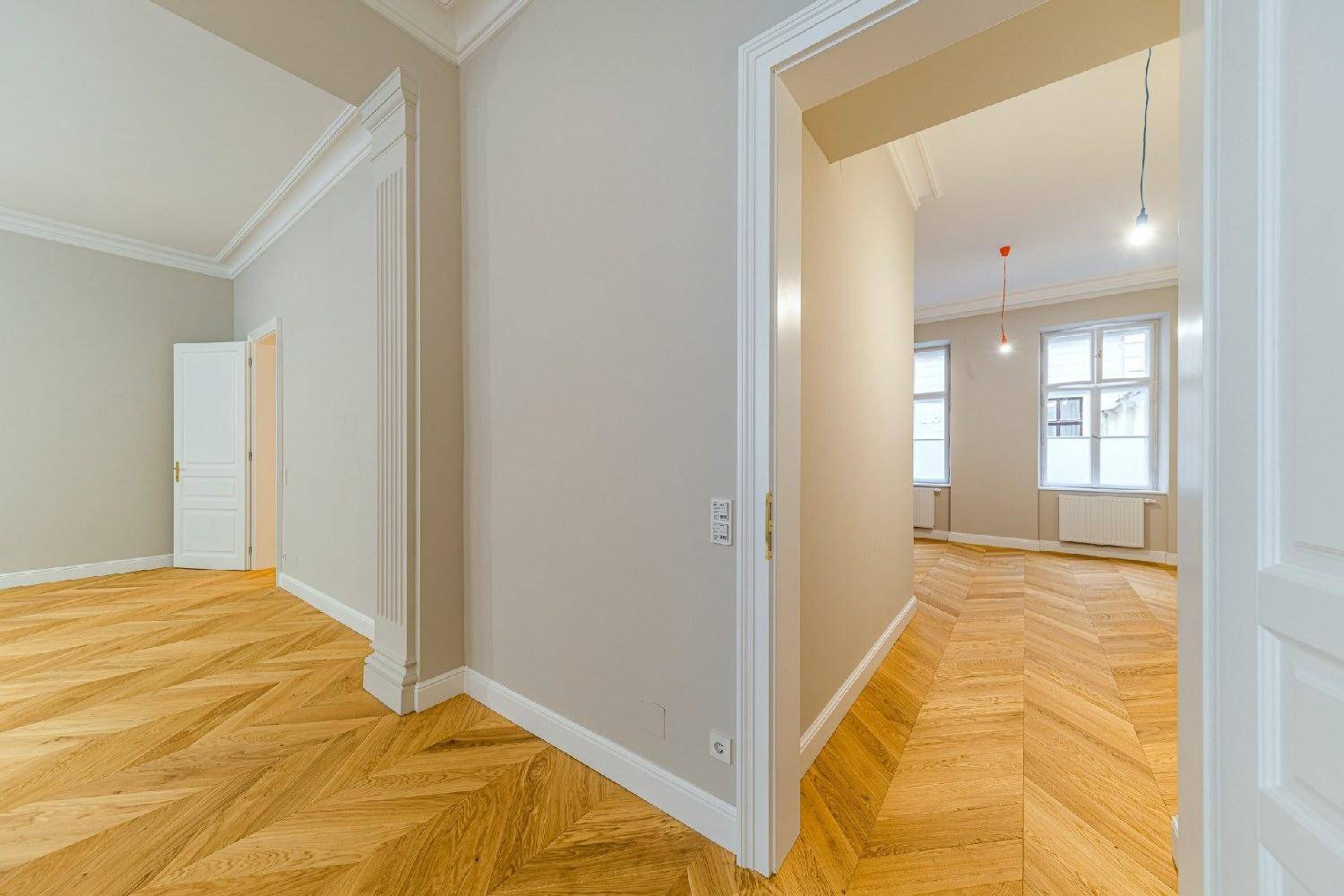 Flur mit Fischgrätparkett und hohen Türen, der zu weiteren hellen Räumen der Wohnung führt.