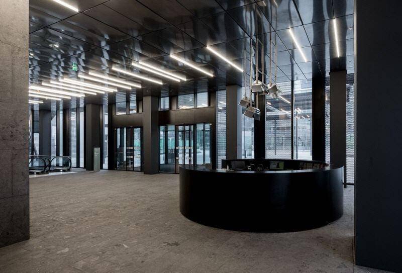 Moderne und elegante Lobby mit einer runden schwarzen Rezeption, hohen Decken und einer beeindruckenden Glasfassade.