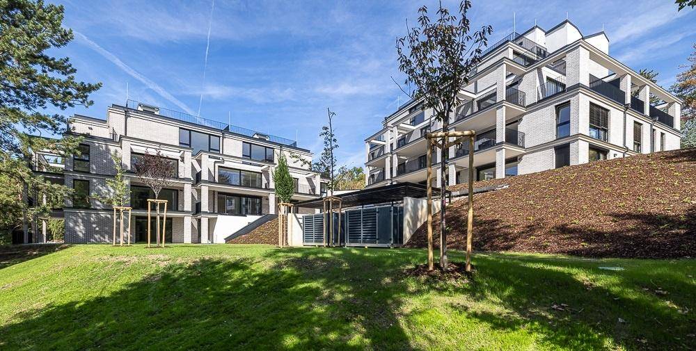 Moderne Wohngebäude mit gestuften Fassaden und großen Balkonen in einer grünen Hanglage.