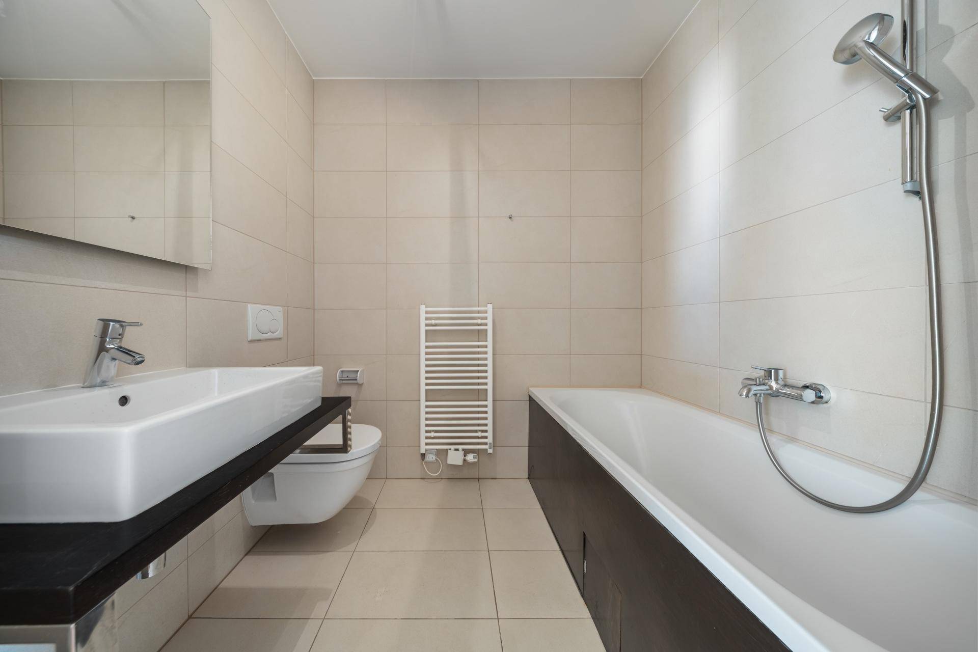 Modernes Badezimmer mit beigefarbenen Fliesen, Badewanne, Einzelwaschbecken und Handtuchheizkörper.