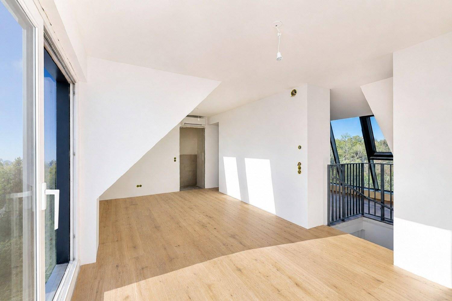 Heller Dachbodenraum mit modernem Laminatboden, großen Fenstern und Zugang zu einem Balkon.