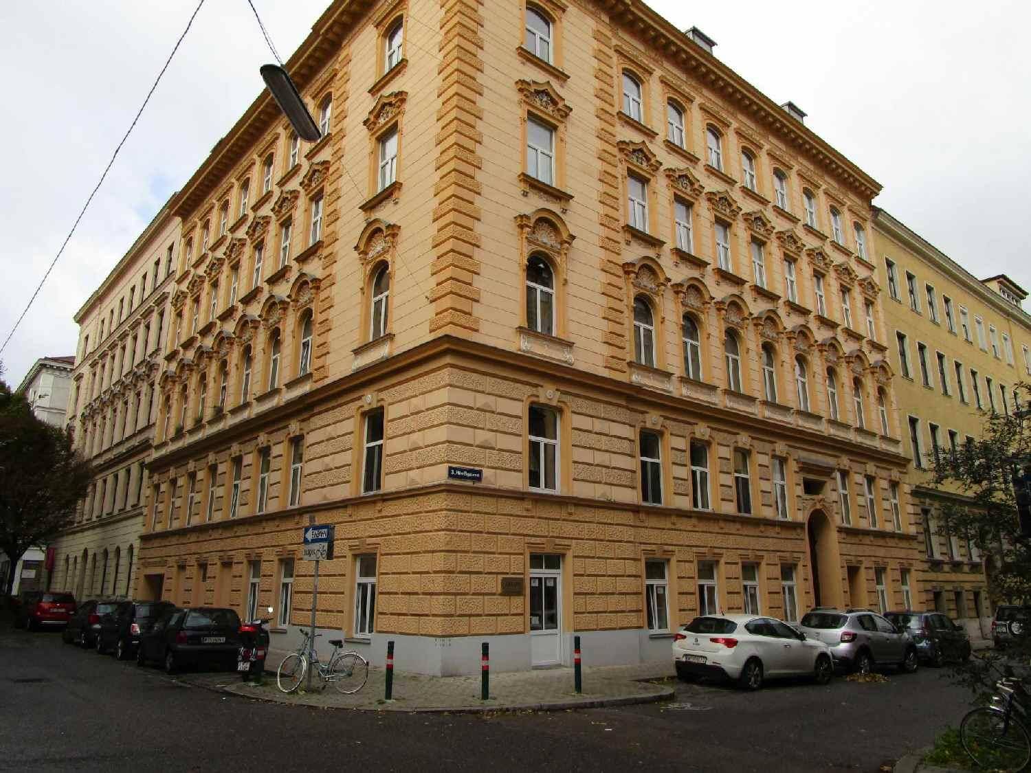 Großes Eckgebäude mit historischer Fassade und vielen Fenstern, gelegen an einer belebten Stadtstraße.