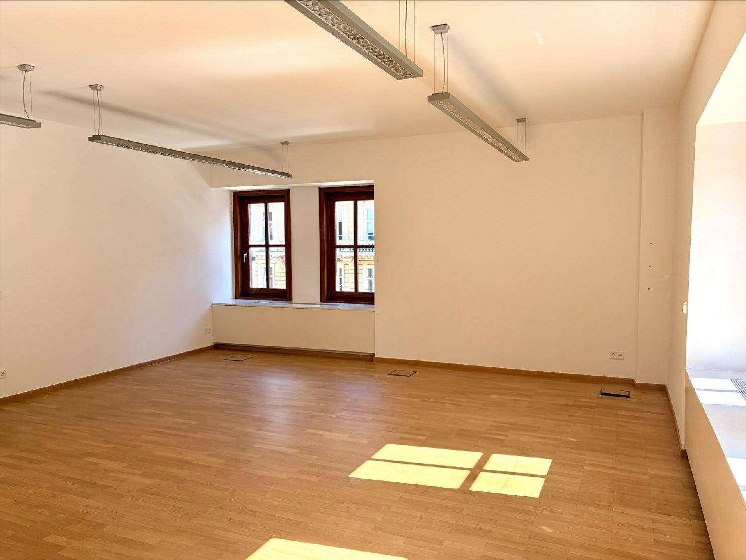 Geräumiger, heller Raum mit Parkettboden und modernen Deckenleuchten, ideal für verschiedene Nutzungen.