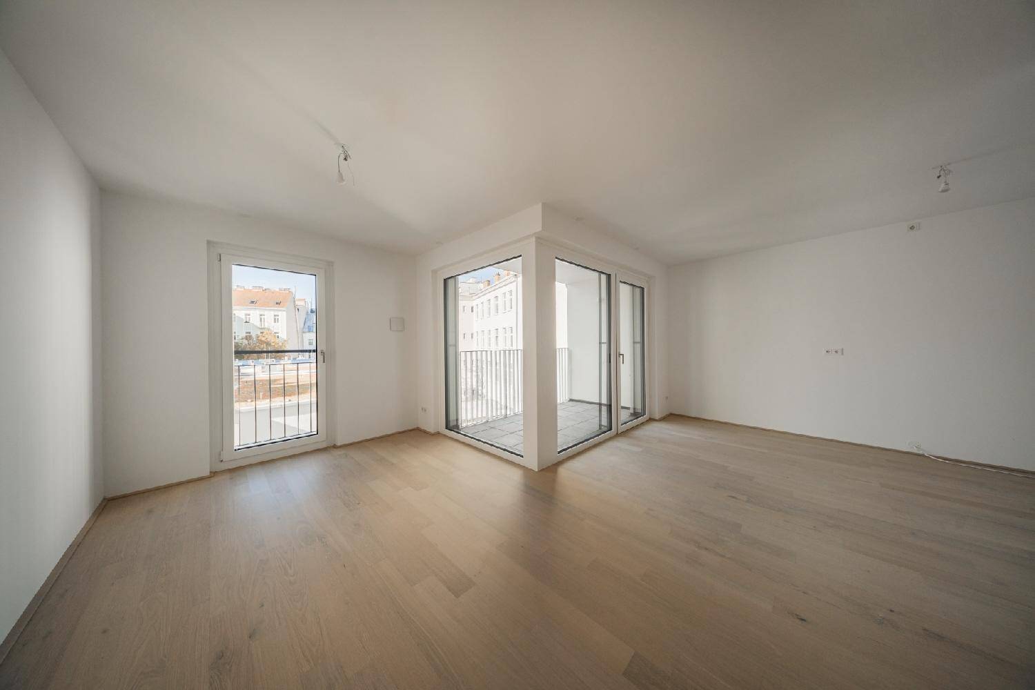 Lichtdurchfluteter Eckraum mit hellen Wänden und Parkettboden, ideal für Wohnbereiche.