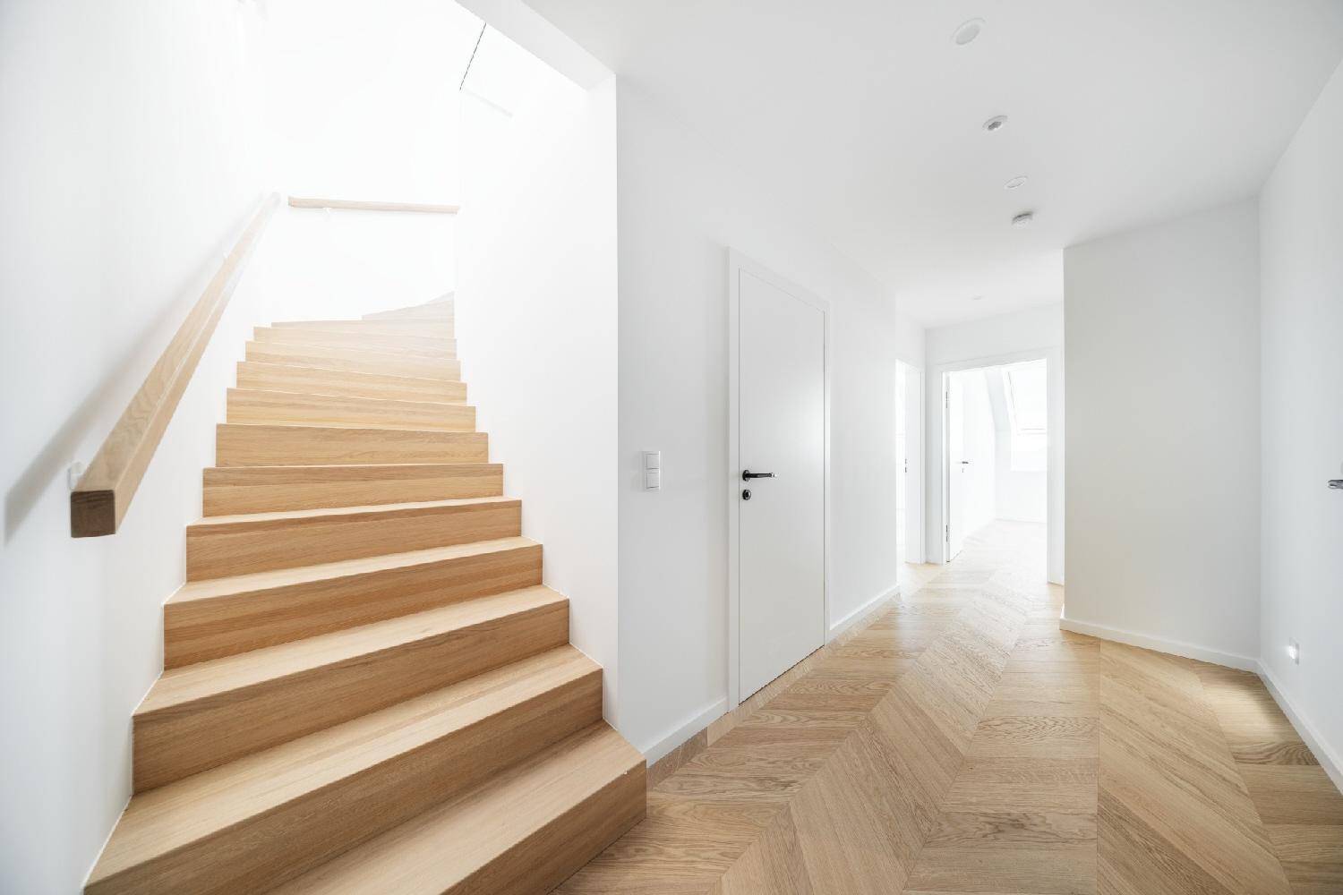 Heller Flur mit einer eleganten Holztreppe und passendem Fischgrätparkettboden.