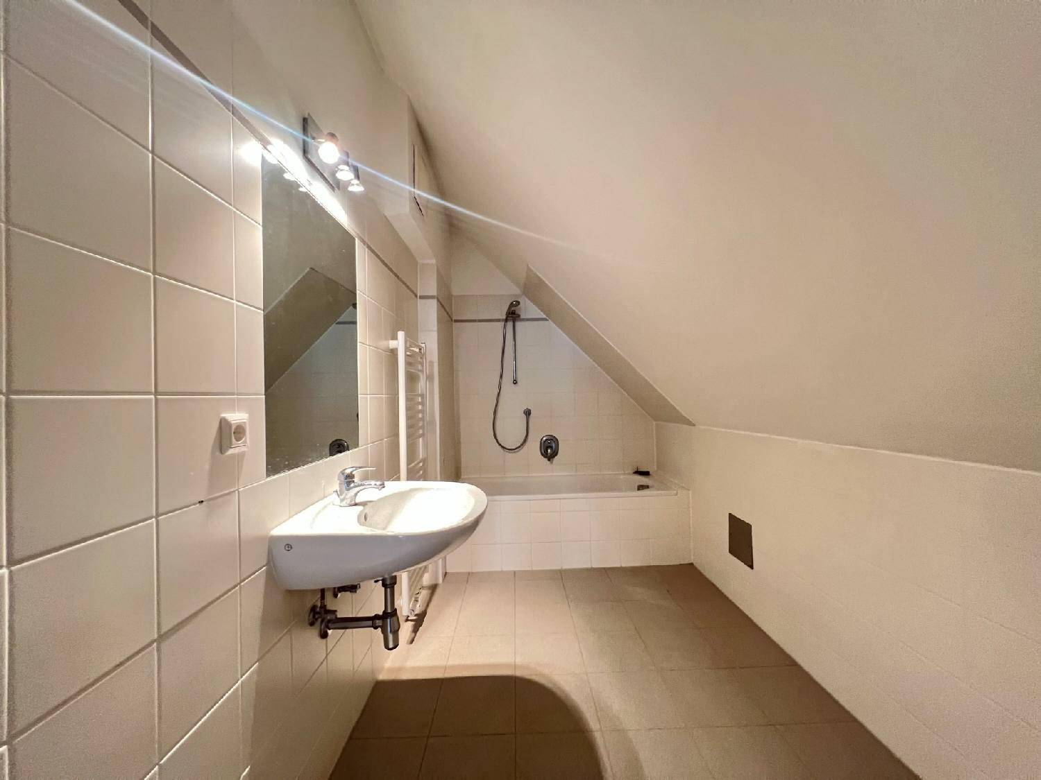 Helles Badezimmer mit Badewanne, Waschbecken und beheiztem Handtuchhalter unter Dachschräge.