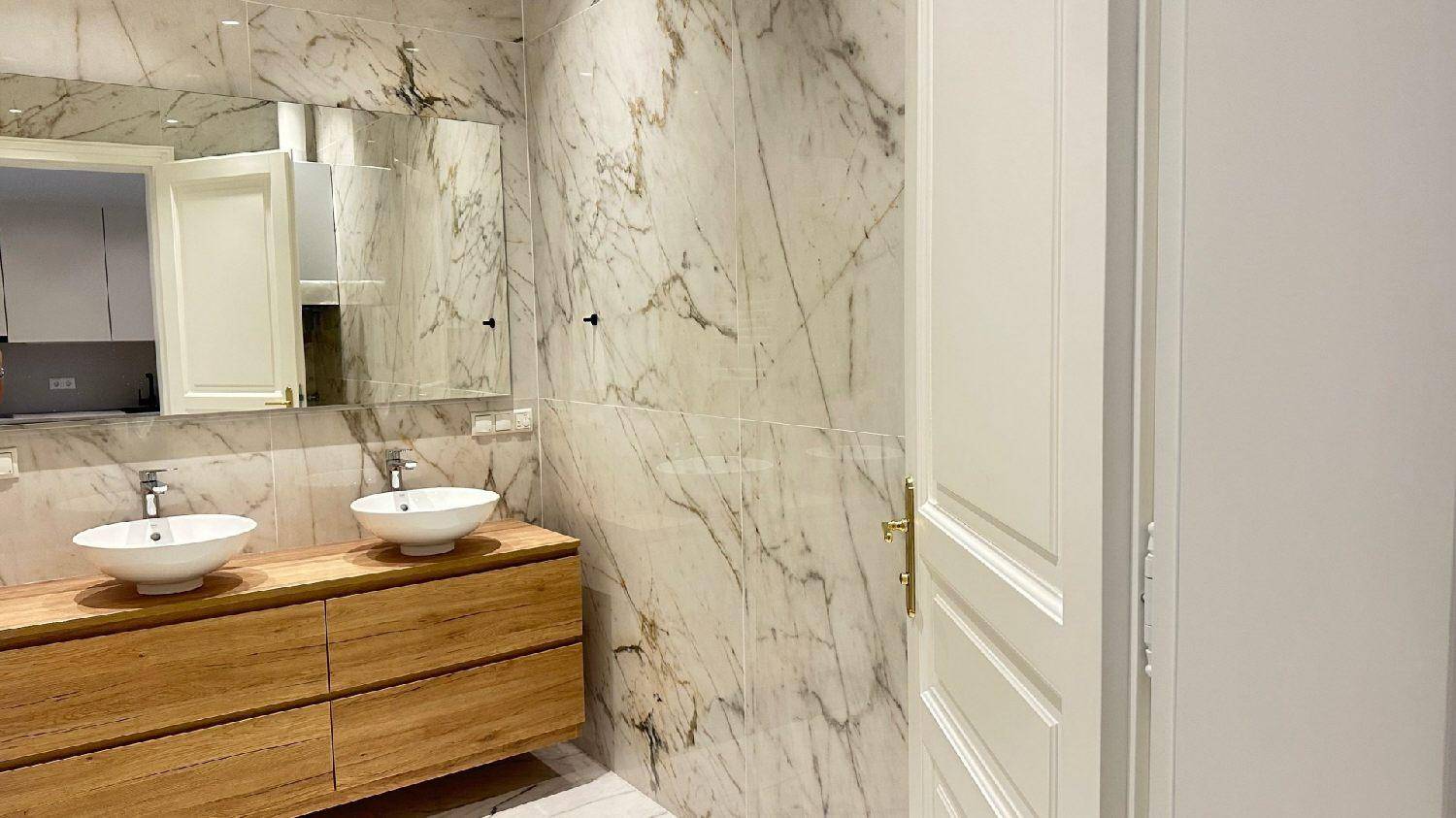 Elegantes Badezimmer mit Marmorwänden, zwei Aufsatzwaschbecken auf Holzunterschrank und großem Spiegel.