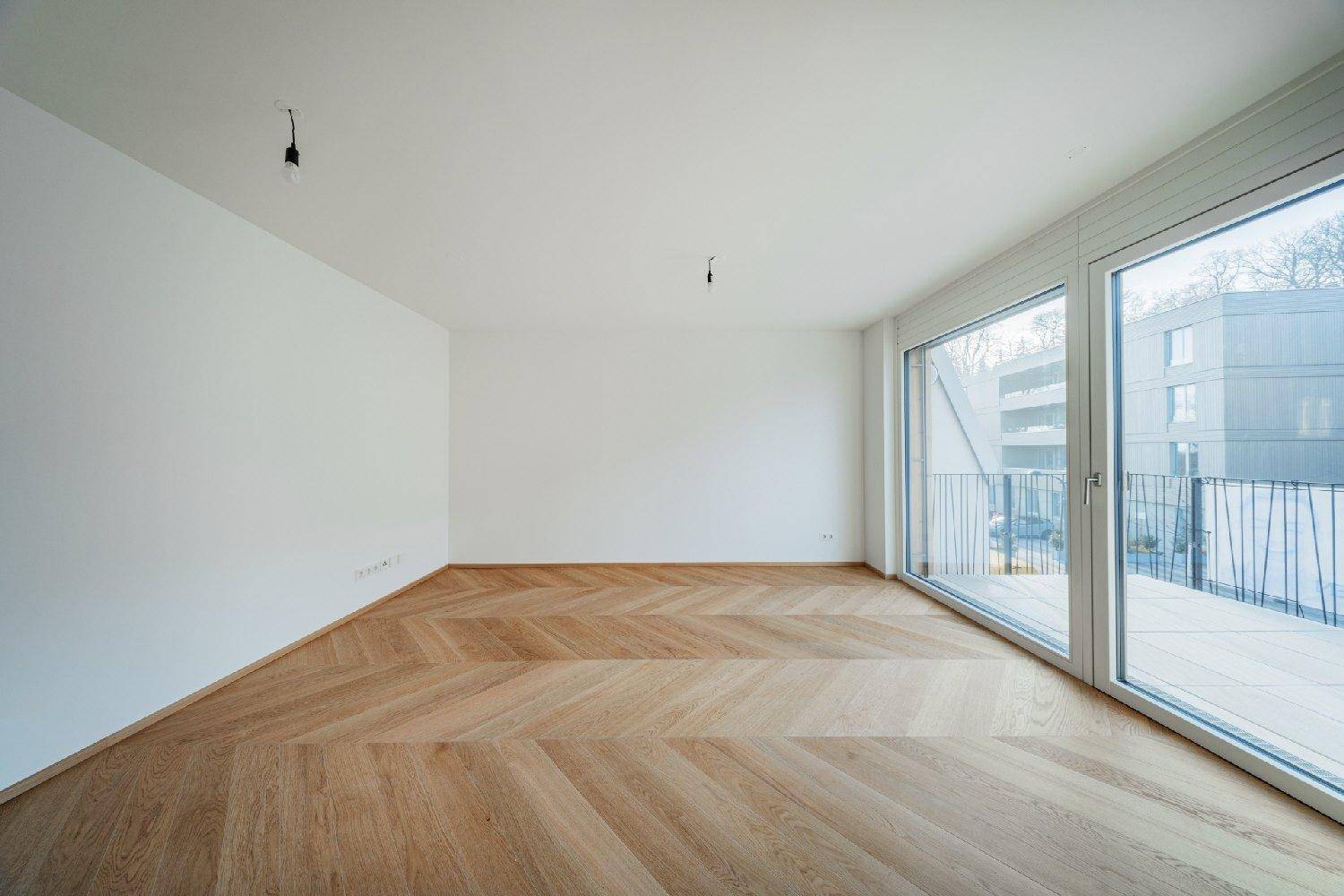 Großzügiger, heller Raum mit Fischgrätparkett und raumhohen Fenstern zum Balkon.