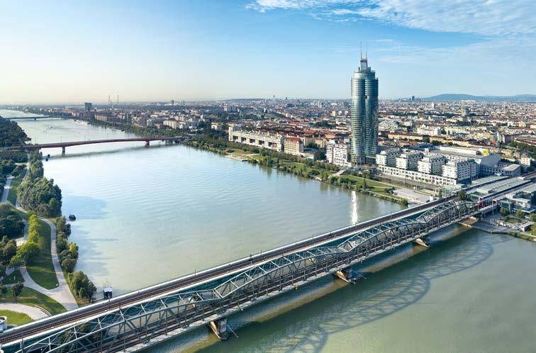 Panoramablick auf eine Stadt mit einem Fluss, Brücken und einem markanten Hochhaus unter klarem Himmel.