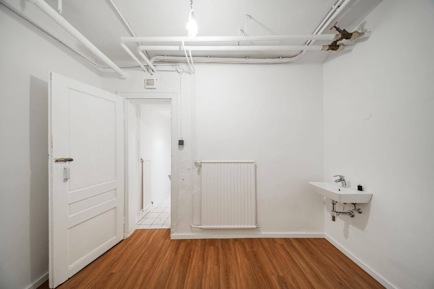 Heller Kellerraum mit Laminatboden und Waschbecken, bietet praktischen Stauraum und Zugang zu einem Bad.