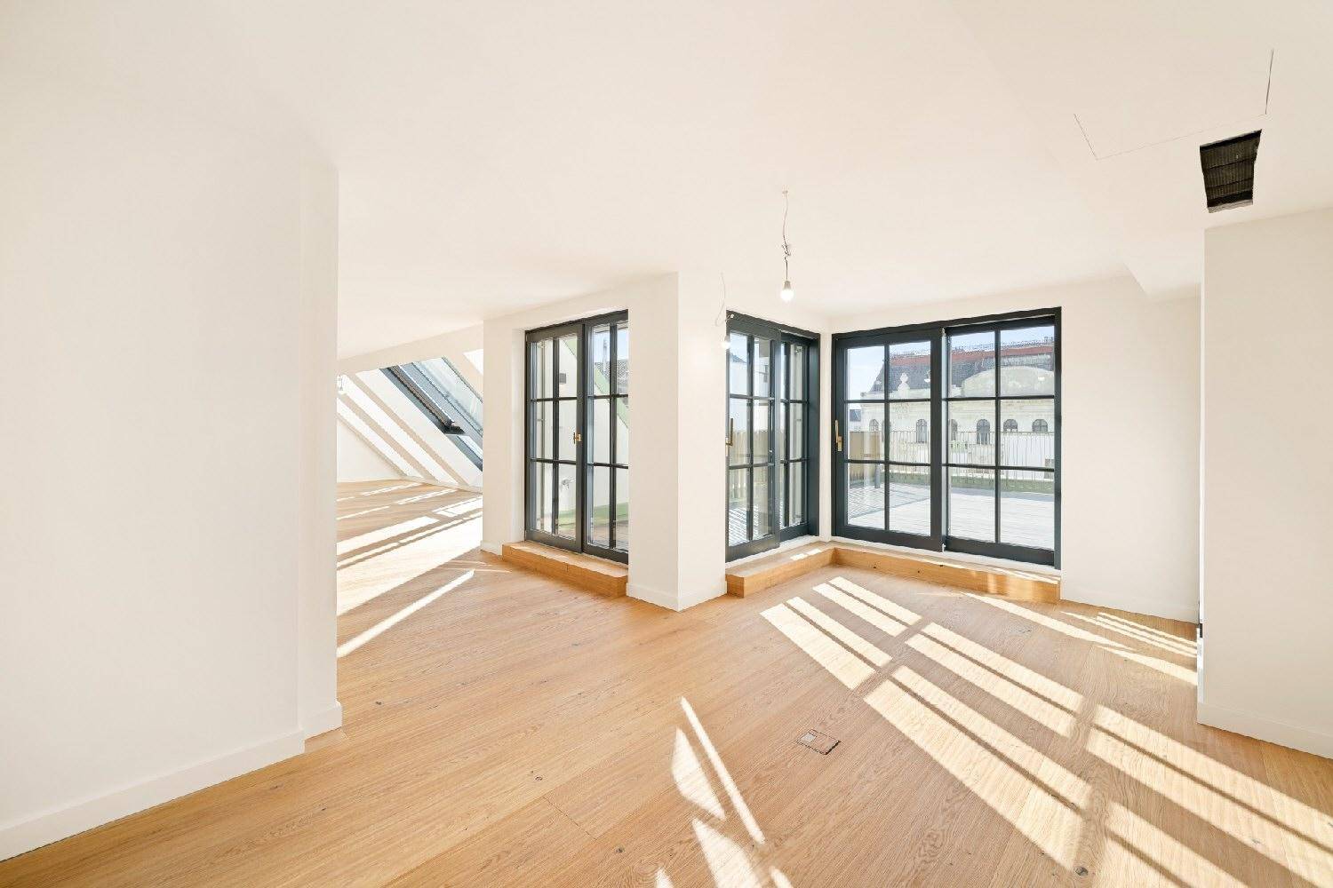 Lichtdurchfluteter Wohnbereich mit großen Fenstertüren und Holzboden, der Zugang nach draußen bietet.