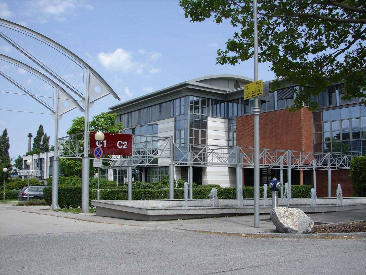 Modernes Bürogebäude mit Ziegelfassade und Glasfronten, umgeben von einem dekorativen Brunnen und Grünflächen.