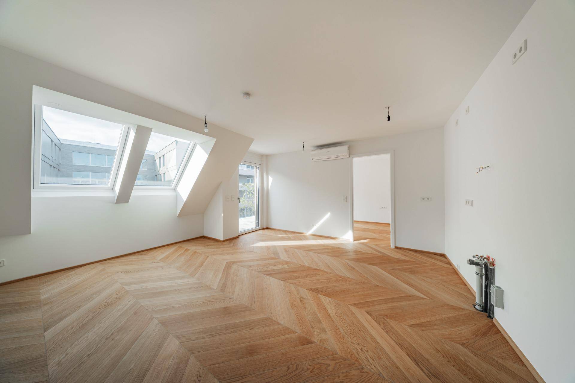 Lichtdurchfluteter Raum mit schrägen Dachfenstern, Fischgrätparkett und Klimaanlage, ideal für ein Schlafzimmer oder Büro.