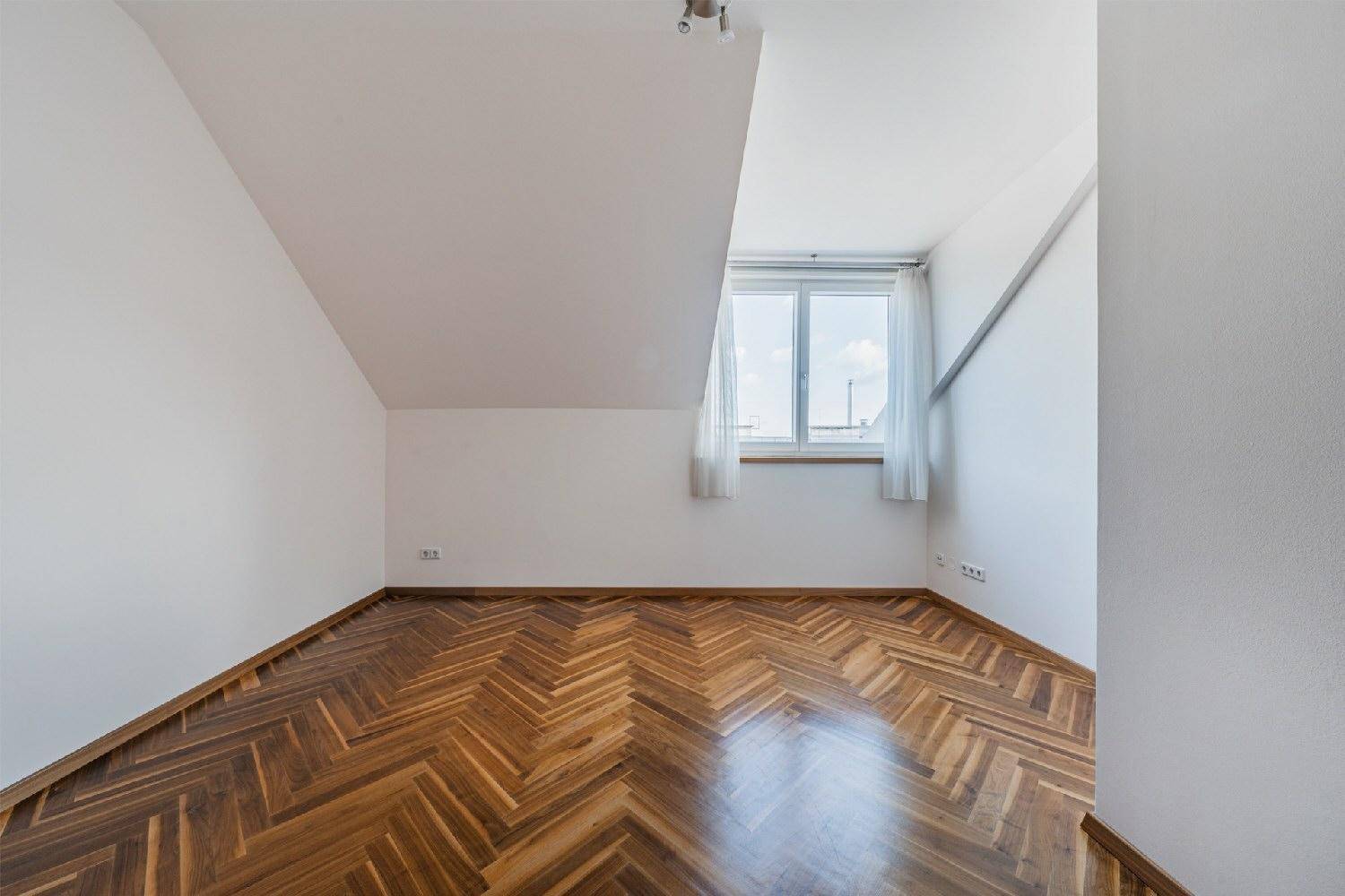 Helles Schlafzimmer mit Dachschräge, Fischgrätparkett und Fenster.