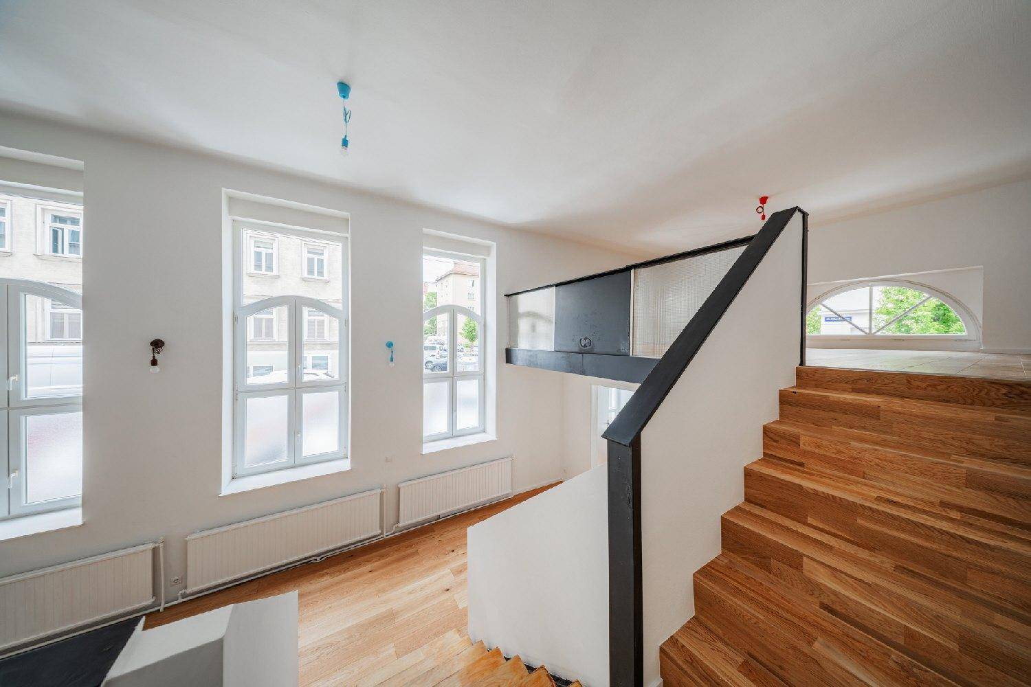 Heller Raum mit Holzboden und Holztreppe zur Galerie, große Fenster bieten viel Licht.