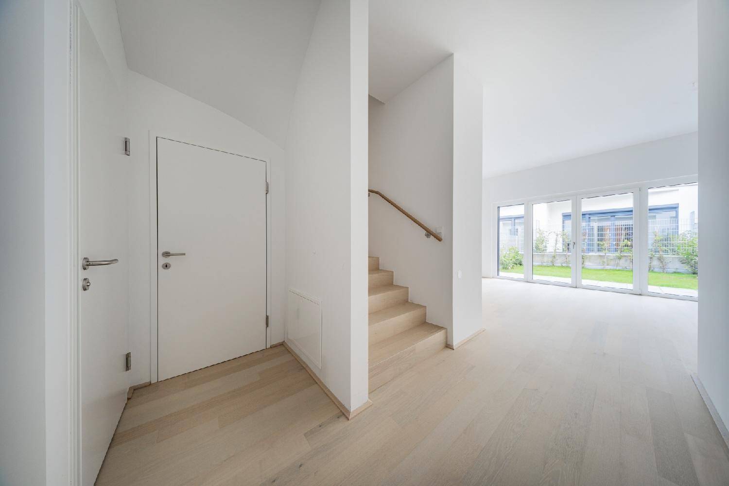 Heller Flur mit Holztreppe und modernen Türen, der zu weiteren Räumen führt.