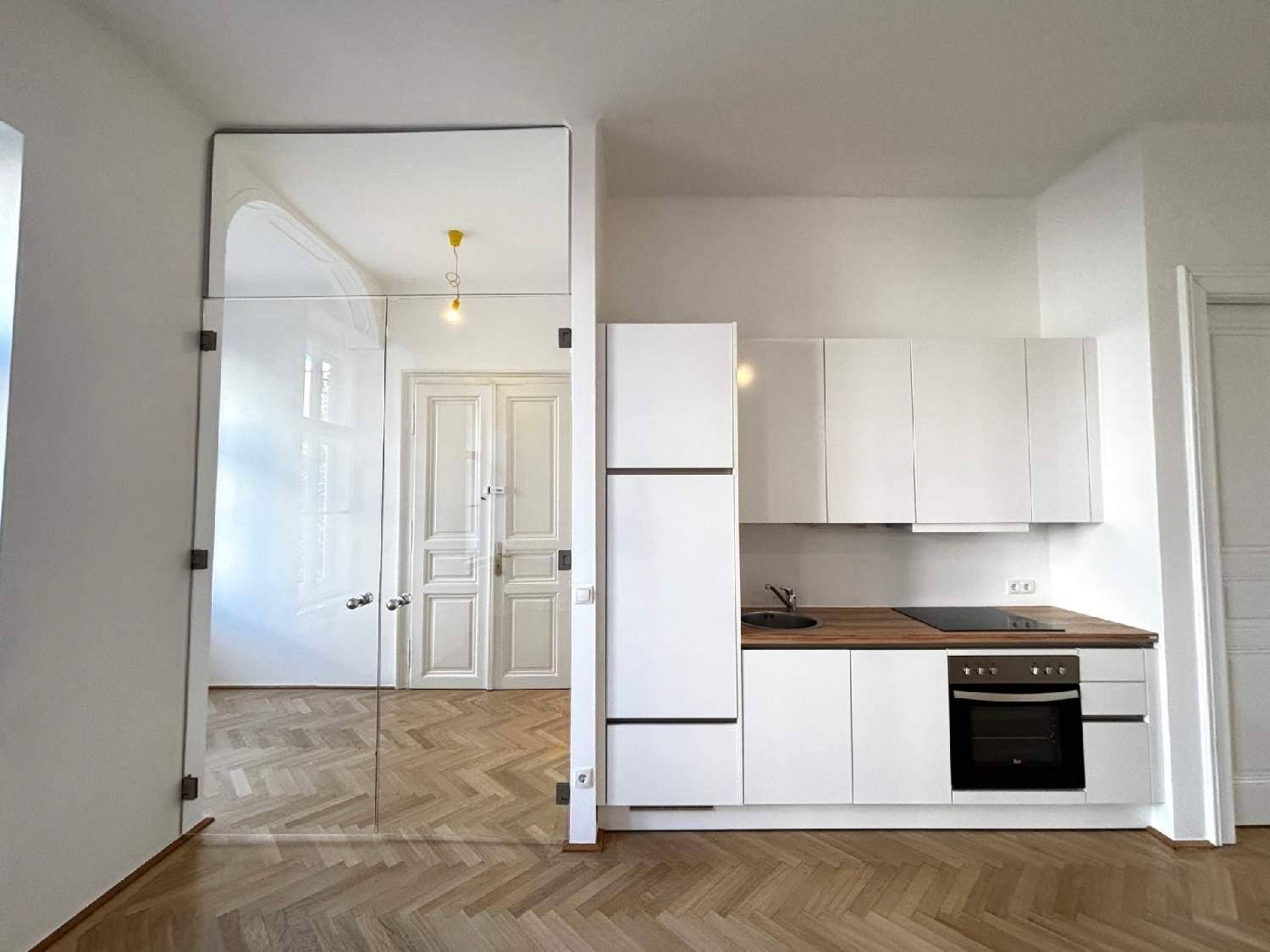 Moderne weiße Küchenzeile mit Holz-Arbeitsplatte und integrierten Geräten neben einer Glaswand.