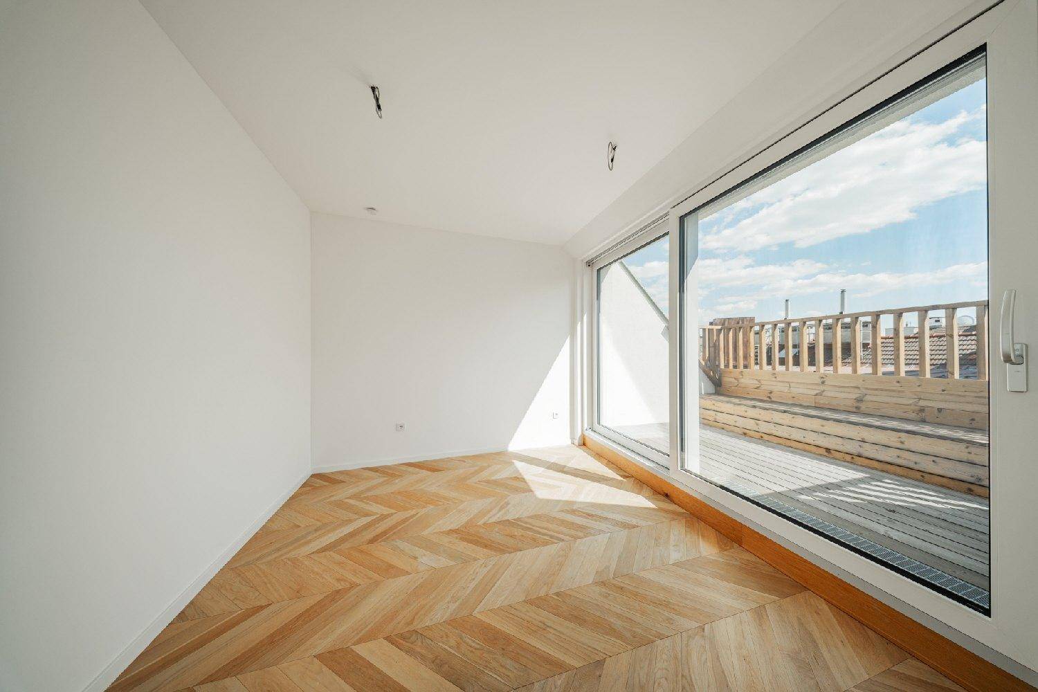 Lichtdurchfluteter Raum mit Fischgrätparkett und Zugang zu einer großen Dachterrasse.