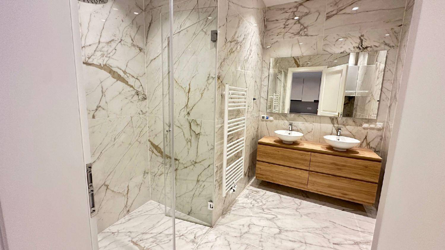 Luxuriöses Badezimmer mit Marmorfliesen, Doppelwaschbecken und einer geräumigen begehbaren Dusche.