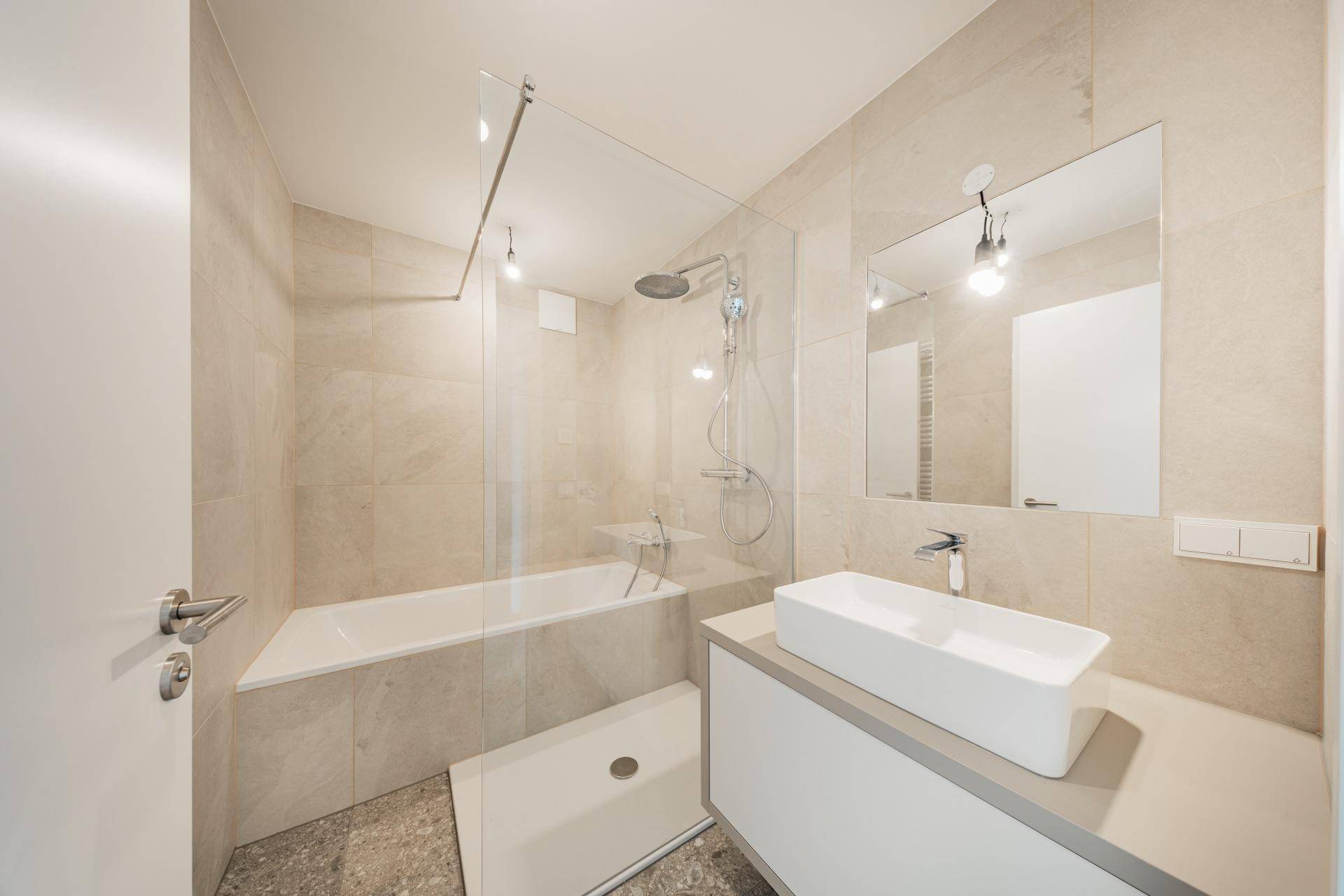 Modernes Badezimmer mit beigefarbenen Fliesen, Badewanne mit Dusche und elegantem Waschbecken.