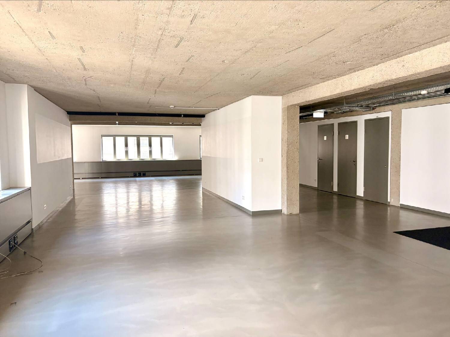 Weitläufiger Bürobereich mit Sichtbetondecke, modernen Fenstern und viel Tageslicht.
