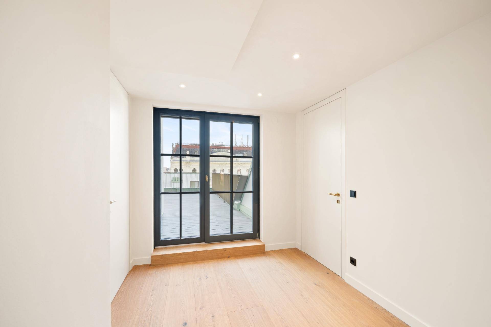 Helles Schlafzimmer mit Holzboden und großen Fenstertüren, die viel Tageslicht hereinlassen.