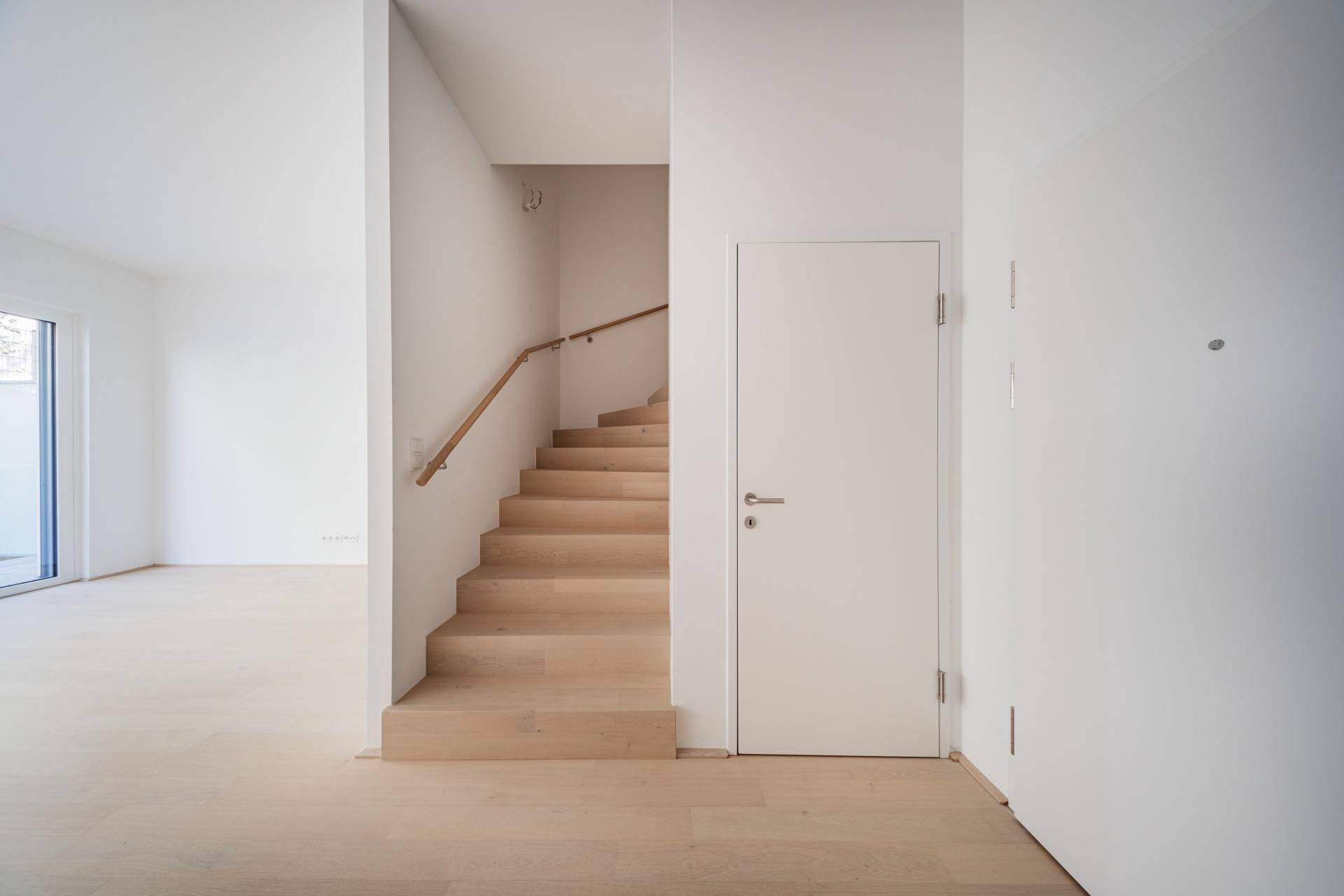 Heller Flur mit Holztreppe und modernen weißen Türen in einem Neubau.