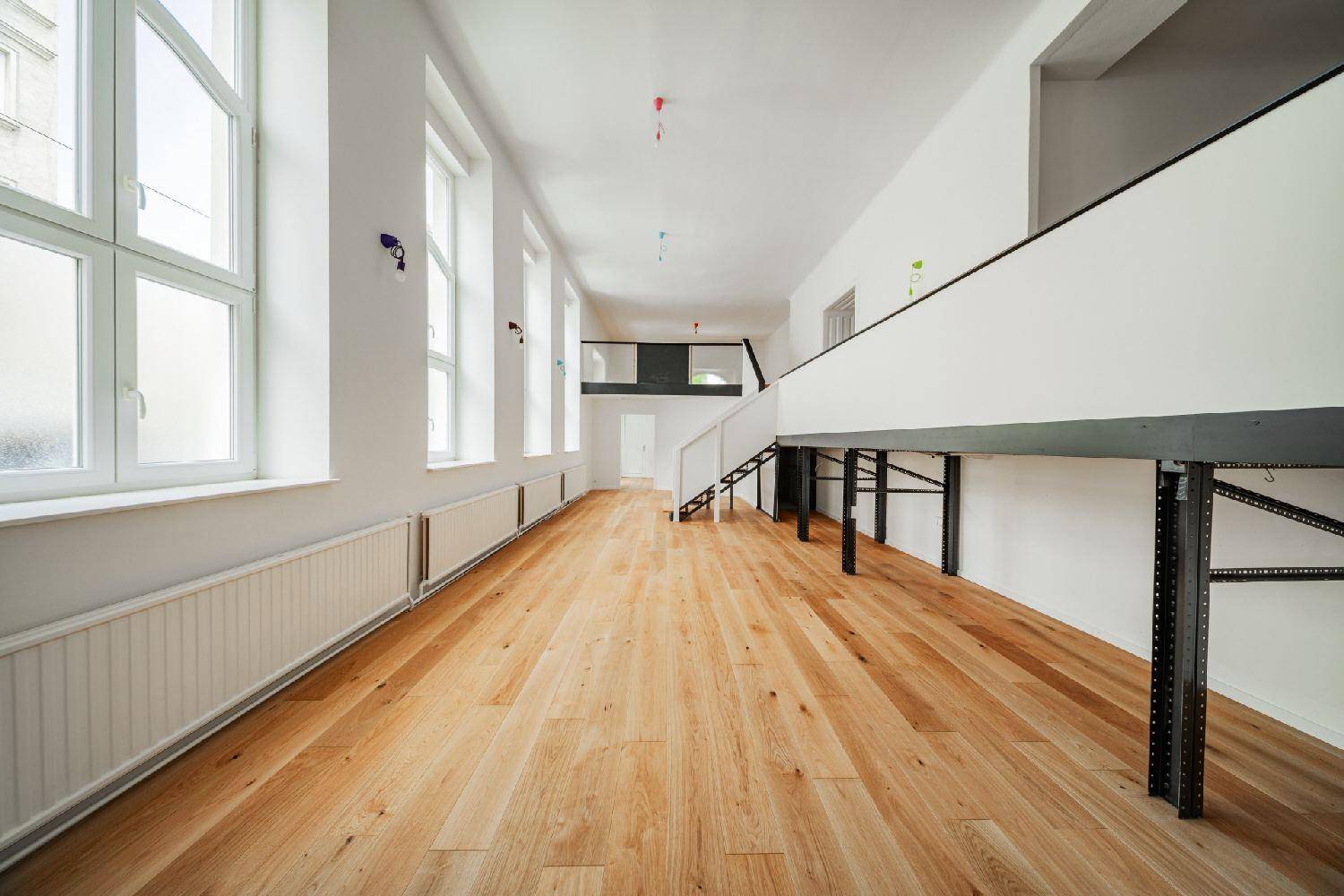 Geräumiger, heller Raum mit Holzboden und einer Galerie, große Fenster sorgen für viel Tageslicht.