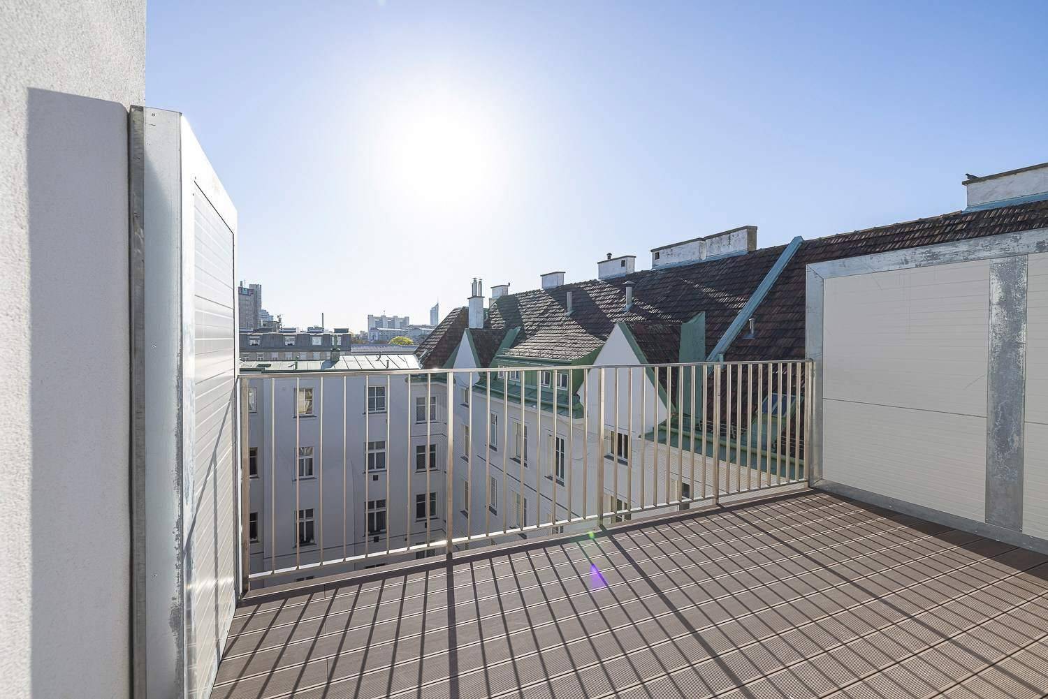 Sonnige Terrasse mit Metallgeländer und weitem Blick über die Dächer der Stadt.