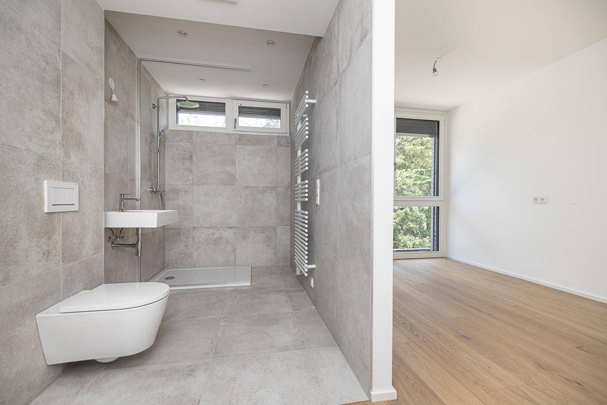 Modernes Badezimmer mit grauen Fliesen, ebenerdiger Dusche und beheiztem Handtuchhalter.