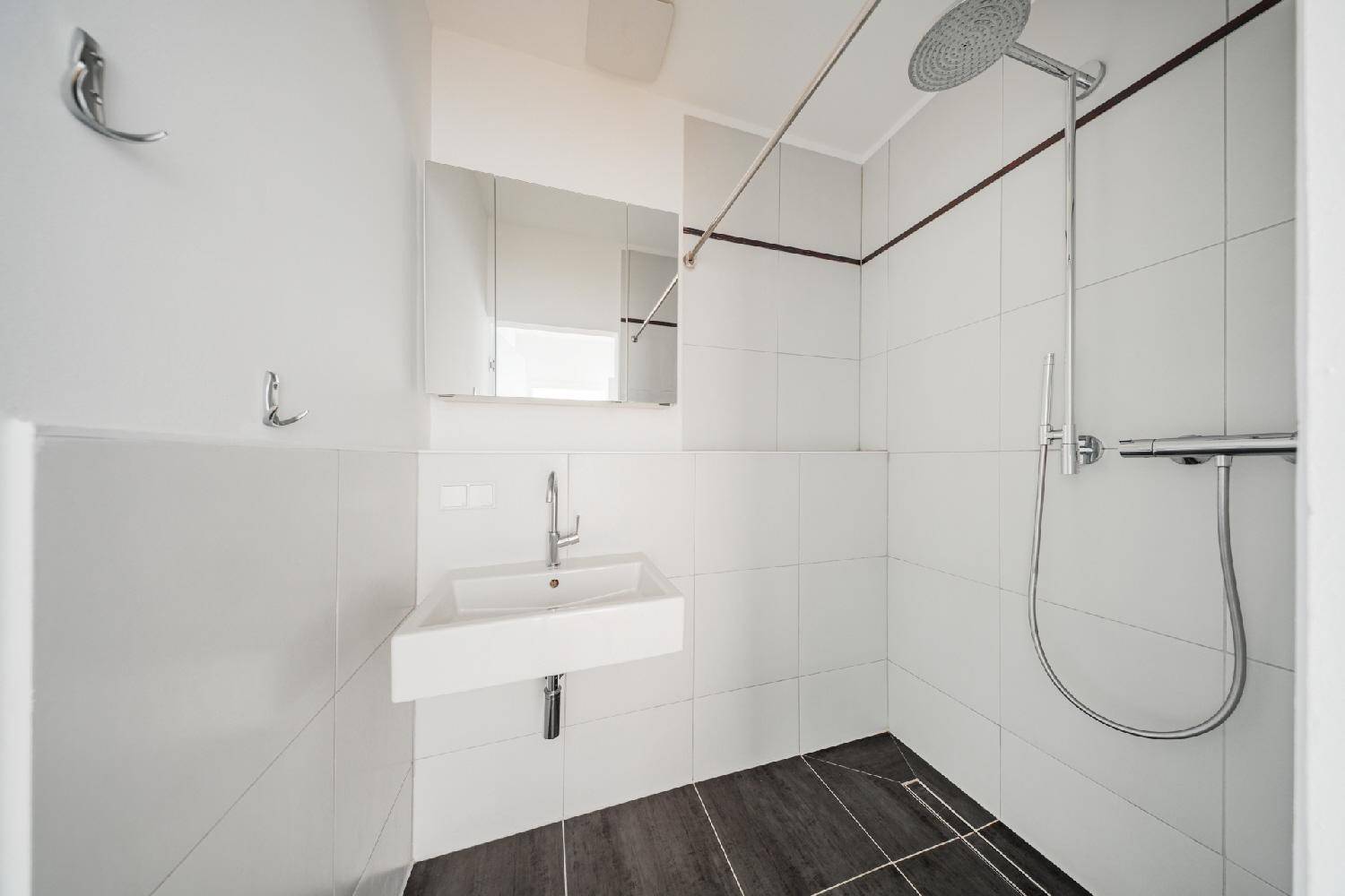 Modernes Badezimmer mit Duschkabine, Waschbecken und weißen Fliesen an den Wänden.