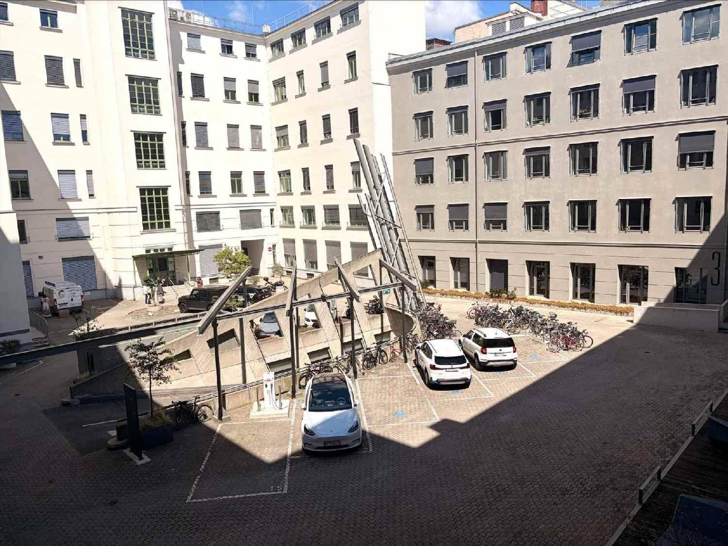 Innenhof mit Parkplätzen, Fahrrädern und Gebäuden im Hintergrund unter blauem Himmel.
