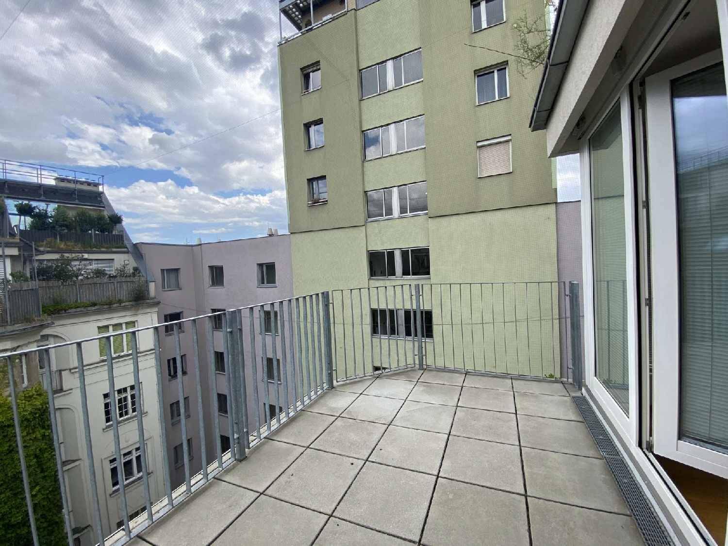 Großer Balkon mit Fliesen und Blick auf die umliegenden Gebäude und den Himmel.