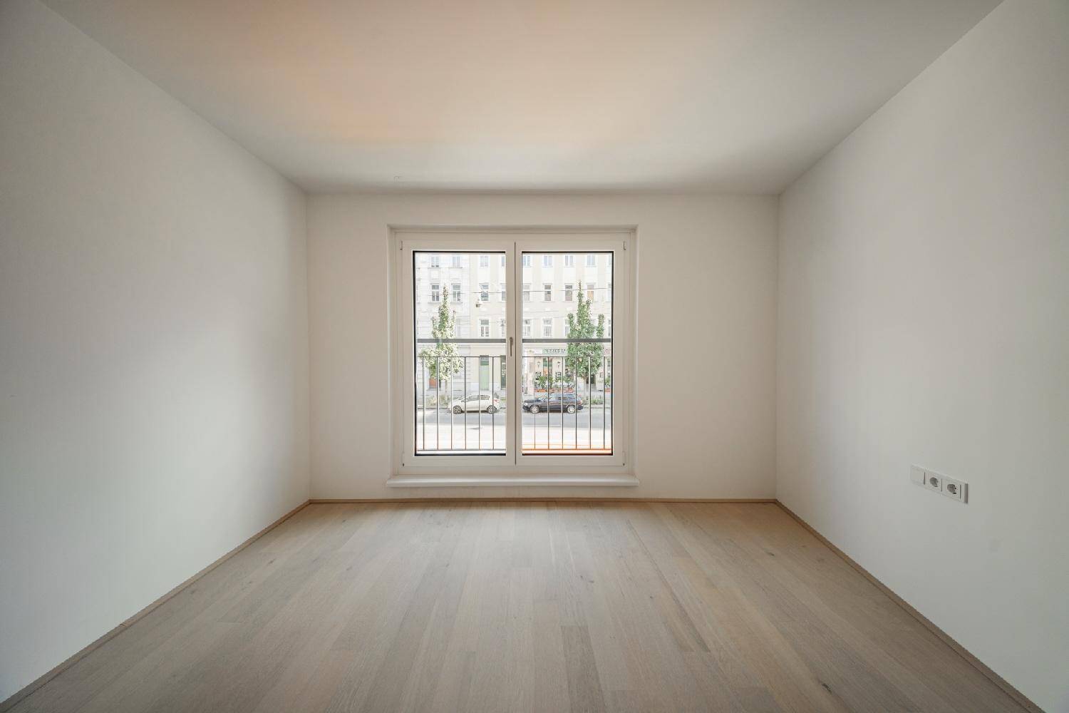 Geräumiges Schlafzimmer mit hellem Holzboden und einem Fenster mit französischem Balkon zur Straße.