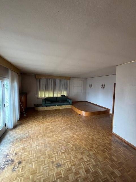Geräumiges Wohnzimmer mit Parkettboden, einem erhöhten Sitzbereich und großen Fenstern.
