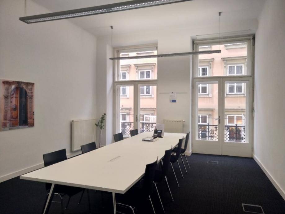 Geräumiger Konferenzraum mit langem Tisch, vielen Stühlen und großen Fenstern, die viel Licht hereinlassen.