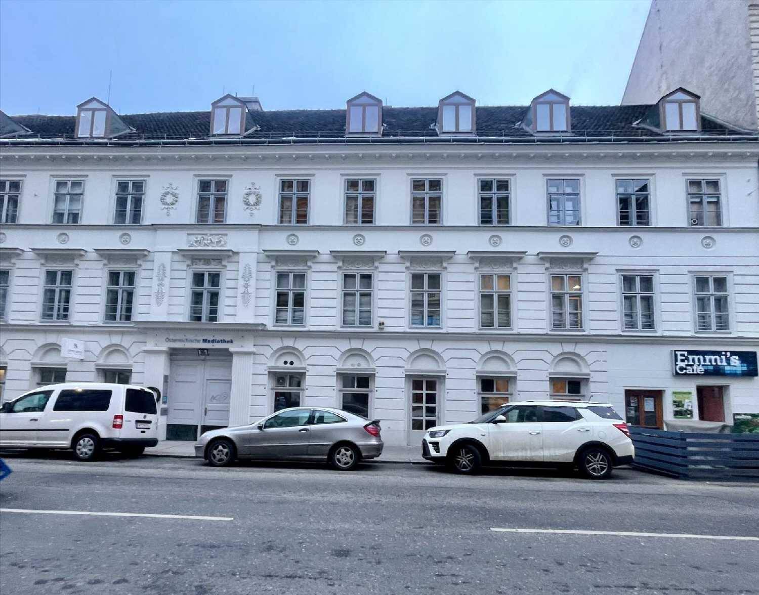 Historische weiße Fassade eines Gebäudes mit vielen Fenstern und Geschäften im Erdgeschoss.