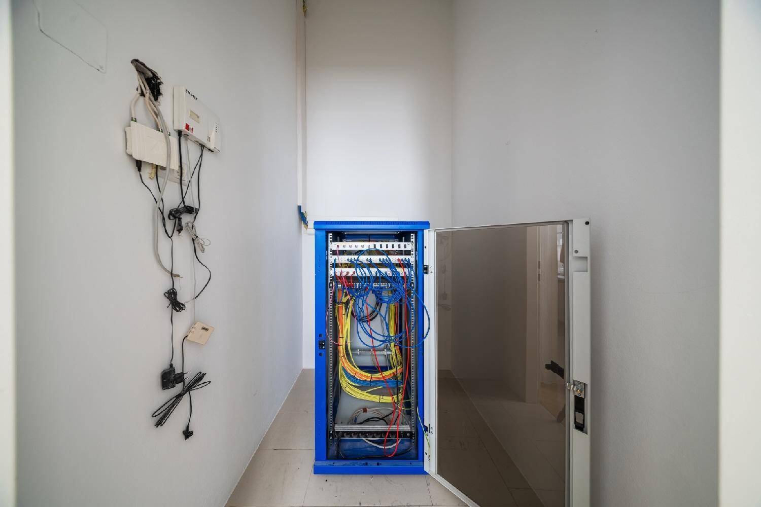 Technikraum mit offenem Serverschrank und Verkabelung an der Wand.
