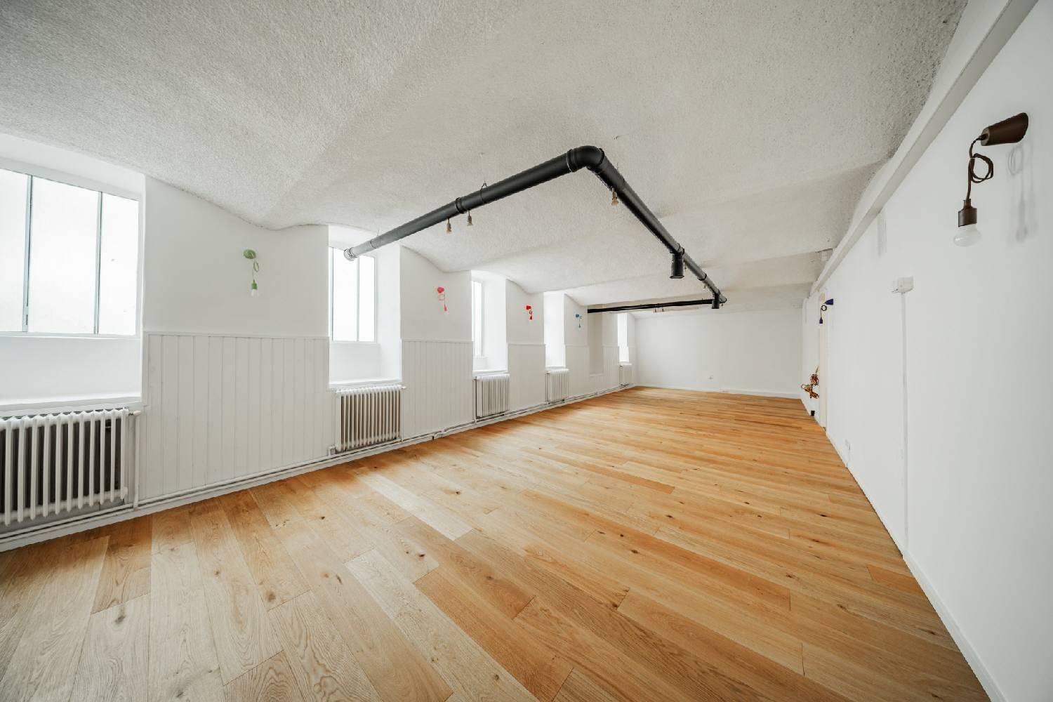 Großer Raum mit Holzboden, strukturierten Decken und sichtbaren Rohren, der vielseitig nutzbar ist.