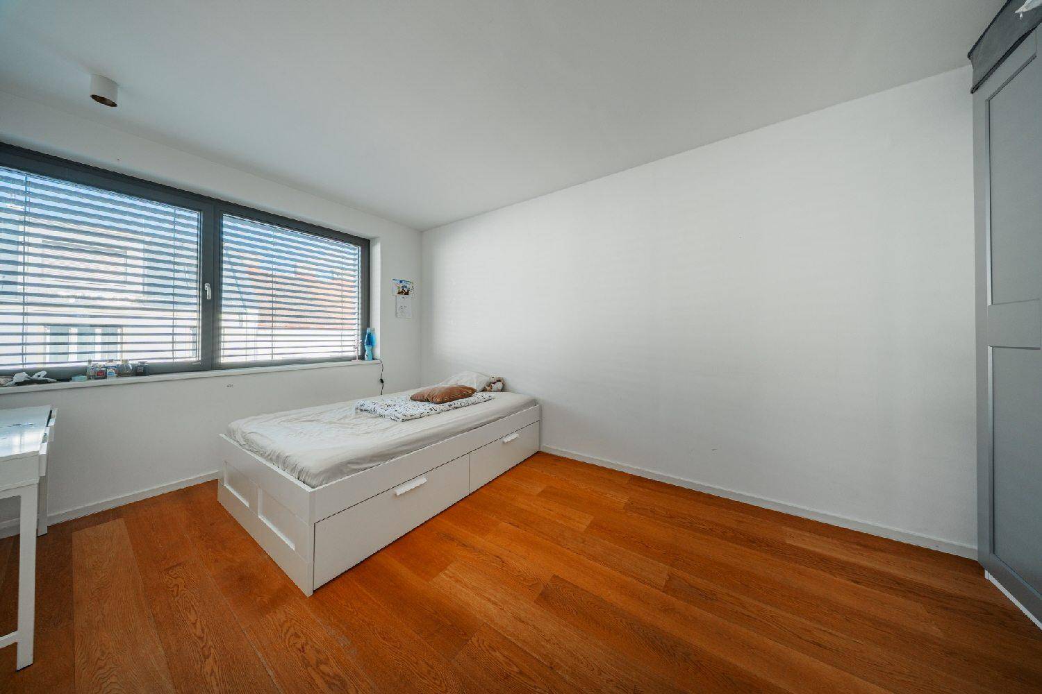 Helles Schlafzimmer mit Holzboden, Einzelbett und großem Fenster mit Jalousien.