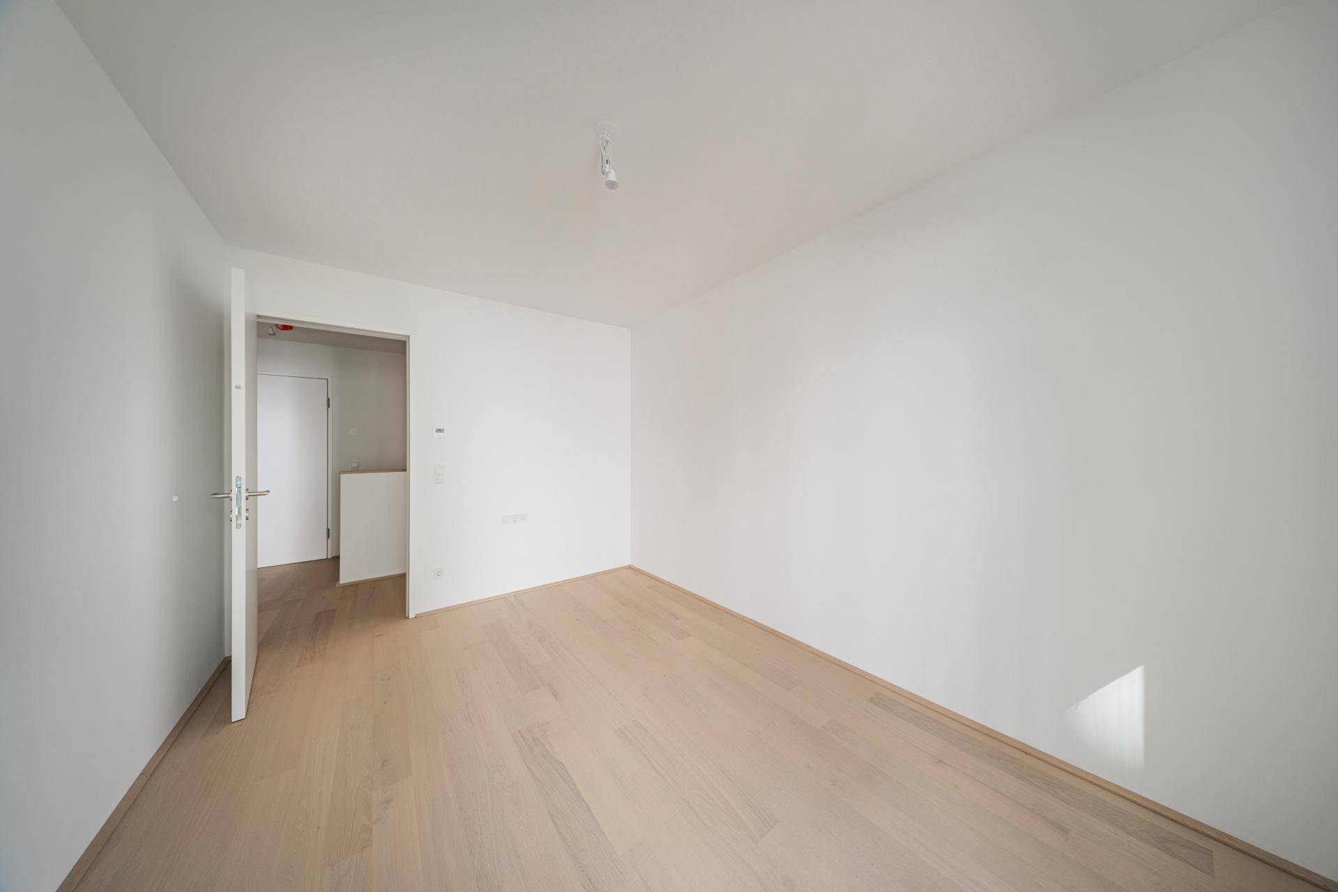 Leeres, helles Zimmer mit Holzboden und Zugang zu einem weiteren Bereich.